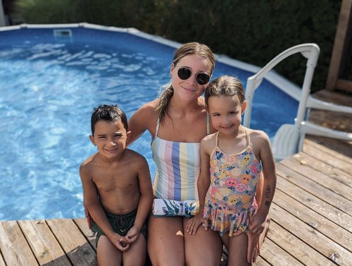 Une monitrice aquatique pose avec 2 enfants lors d'un cours de natation à domicile au bord d'une piscine hors terre