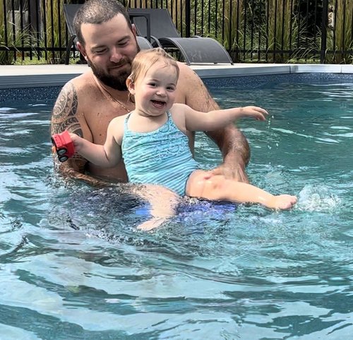 Un papa et sa petite fille dans un maillot une pièce bleu joue dans la piscine