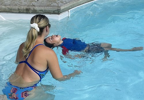 Une monitrice aquatique dans son maillot une pièce bleu montre à son élève à nager sur le dos dans une piscine creusée
